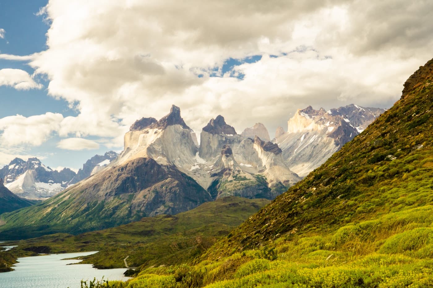 The granite horns of Torres del Paine above a turquoise lake, with green hills in the foreground